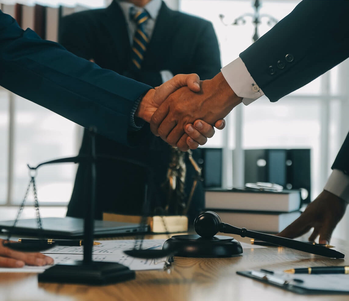 Handshake between attorneys finalizing estate plan, with gavel and legal books on desk